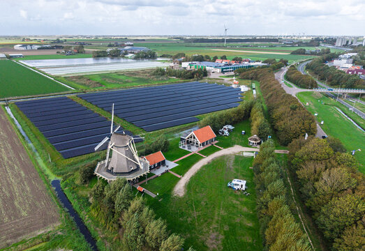 Aerial view of Molen De Hoop windmill situated next to a large solar panel field and green landscape in 't Zand, North Holland, Netherlands.