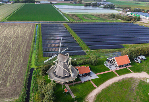 Aerial view of Molen De Hoop windmill surrounded by a large solar farm and green agricultural fields in 't Zand, North Holland, Netherlands.