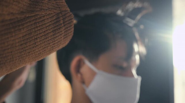 A barber cuts a seated customer&rsquo;s dark hair with scissors during a haircut. The barber holds a comb near the head while the customer wears a face mask and protective cape inside the salon.