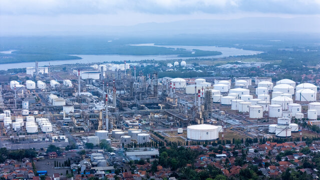 Aerial view of the Pertamina oil refinery complex with numerous large white storage tanks, industrial processing units, and tall chimneys, Cilacap, Central Java, Indonesia.