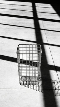 Empty wire shop basket on a polished concrete floor casting a long grid shadow