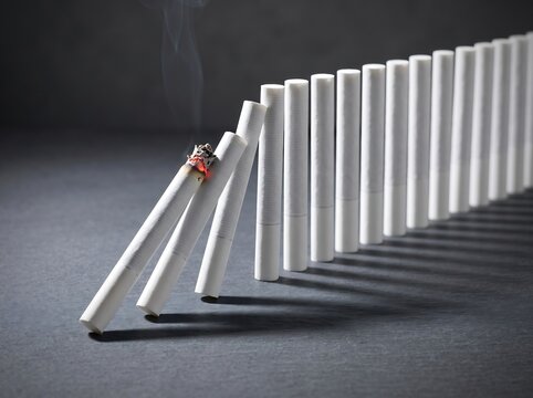 Row of cigarettes falling like dominoes with the first one burning, representing the chain reaction and health risks of smoking