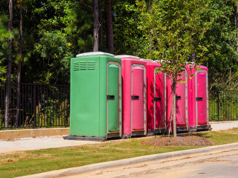 A line of colorful portable toilets lined up outdoors near a tree and fence. Ideal for construction sites, outdoor events, festivals, and sanitation service marketing campaigns.