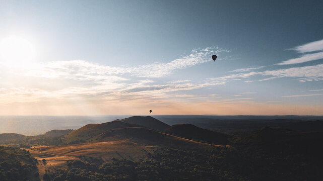 Aerial view of Puy de Dome with hot air balloons floating over the volcanic landscape during golden hour in Orcines, Auvergne-Rhone-Alpes, France.