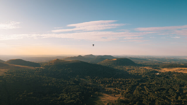 Aerial view of a hot air balloon floating over the volcanic landscape of Puy de Dome at golden hour in Orcines, Auvergne-Rhone-Alpes, France.