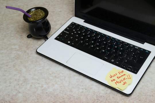 White laptop with colorful motivational sticky notes reading Just Put On Some Music and Keep It Simple, with traditional Argentinian mate cup and colorful markers on a desk. Cozy home office and remot