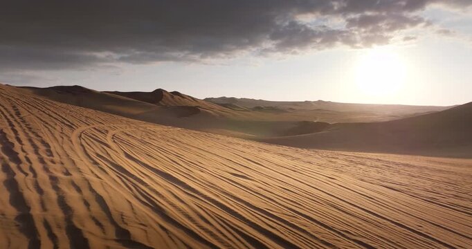 Desert dunes under sunset sky with tire tracks on sand at sunset.