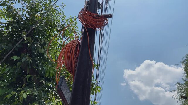 Messy electrical wires and optical fiber cables tangled on a utility pole, illustrating power infrastructure and telecommunications in a low-angle outdoor shot.