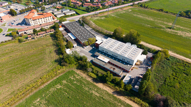 Aerial view of an industrial paint production facility with large warehouse buildings and flat roofs surrounded by green fields in Milan, Lombardy, Italy.