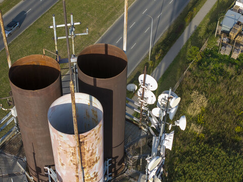 Aerial view of a telecommunications tower featuring large rusted metal pipes and multiple satellite dishes, situated near a road in Krakow, Lesser Poland Voivode, Poland.