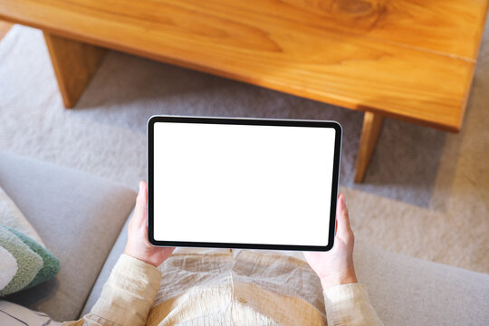 Top view mockup image of a woman holding tablet with blank desktop white screen at home