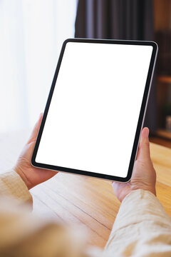 Vertical mockup image of a woman holding tablet with blank desktop white screen at home