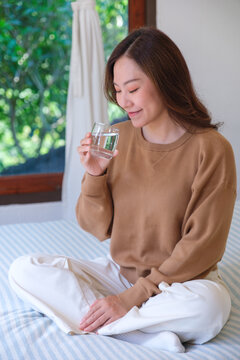 Vertical portrait image of a woman holding and drinking water on the bed at home