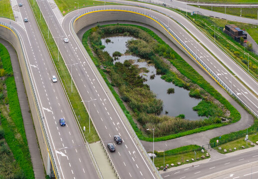 Aerial view of a highway interchange with a U-turn loop and a small pond in the center, surrounded by green grass and concrete walls in Gdansk, Pomeranian Voivodeship, Poland.