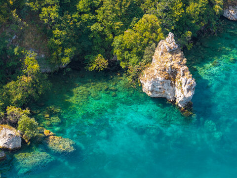 Aerial view of Lake Ohrid with its clear turquoise water, rocky shoreline, and lush green trees in Ohrid, Municipality of Ohrid, North Macedonia.