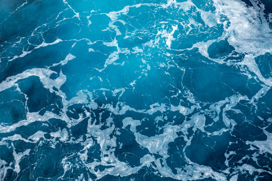 Blue ocean surface with gentle ripples and sparkling sunlight reflections, creating a calm, serene natural background with beautiful water texture.