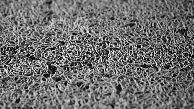 Close-up black and white texture of a woven rubber mat, showcasing intricate interlaced fibers and surface detail for design or background use, highlighting daily-life elements.