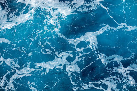 Blue ocean surface with gentle ripples and sparkling sunlight reflections, creating a calm, serene natural background with beautiful water texture.
