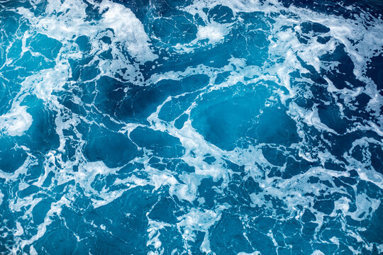 Blue ocean surface with gentle ripples and sparkling sunlight reflections, creating a calm, serene natural background with beautiful water texture.