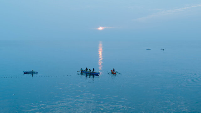 Aerial view of fishermen in traditional outrigger boats on the calm sea at sunrise in Dumaguete City, Negros Island Region, Philippines.