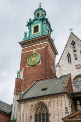 Wawel Cathedral's prominent Sigismund Clock Tower, featuring an ornate green and gold clock face, and a section of the grand Gothic facade in Krakow, Poland. © Danica Chang