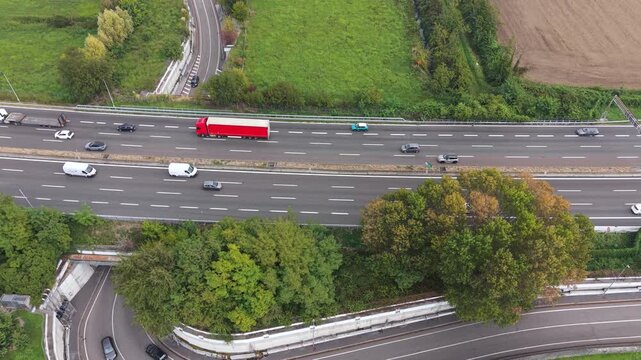 Highway Traffic Flow: An aerial view captures the steady stream of vehicles, including a prominent red truck, navigating a multi-lane highway amidst a backdrop of green fields and trees.