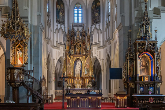The expansive interior of St. Joseph's Church showcases its main gilded altar, ornate pulpit, and elegant vaulted ceilings on a solemn afternoon in Krakow, Poland.