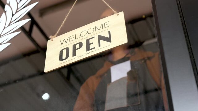 A closed sign hangs on the glass door of a barbershop. The barbershop entrance shows a hanging placard, storefront window, reflected light, and dark lettering against the clear glass.