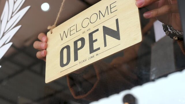 A closed sign hangs on the glass door of a barbershop. The barbershop entrance shows a hanging placard, storefront window, reflected light, and dark lettering against the clear glass.
