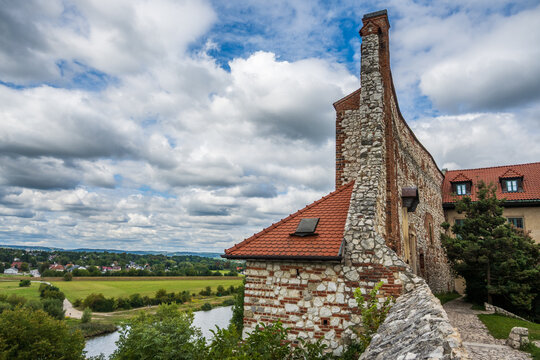 Medieval stone and brick abbey building with red tile roof and chimney, situated above a winding river and fertile fields at Benedictine Abbey in Tyniec, Krakow, Poland.