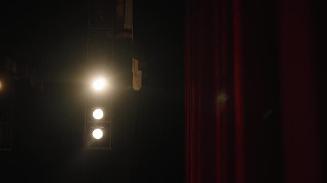 Dark theater interior with warm stage lights beside a red curtain as the camera moves right until the curtain covers the frame.