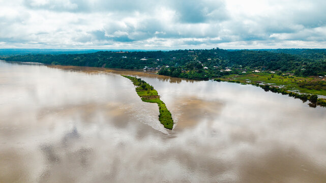 Aerial view of the Cross River with a small green island and lush riverbanks under a cloudy sky in Itu, Akwa Ibom, Nigeria.
