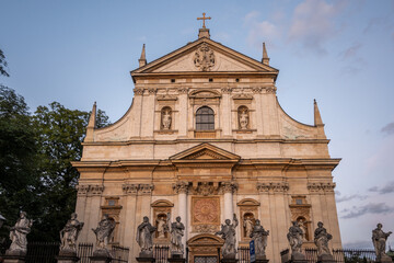 The magnificent Baroque facade of Saints Peter and Paul Church showcases ornate columns, arches, and a series of saints' statues along a fence in Krakow, Poland. © Danica Chang