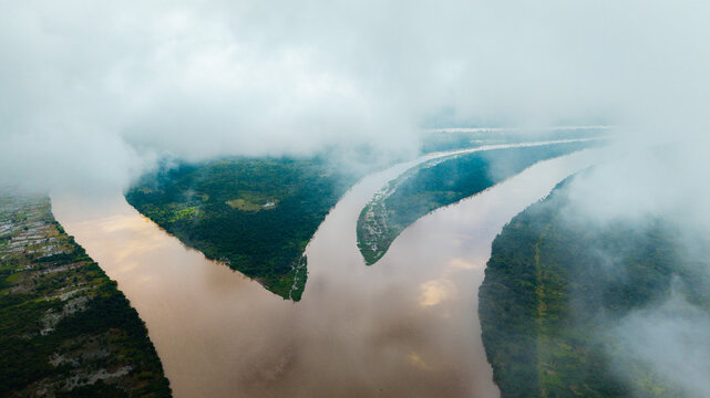 Aerial view of the confluence of the Cross River and Calabar River surrounded by lush green vegetation and low-hanging clouds in Itu, Akwa Ibom, Nigeria.
