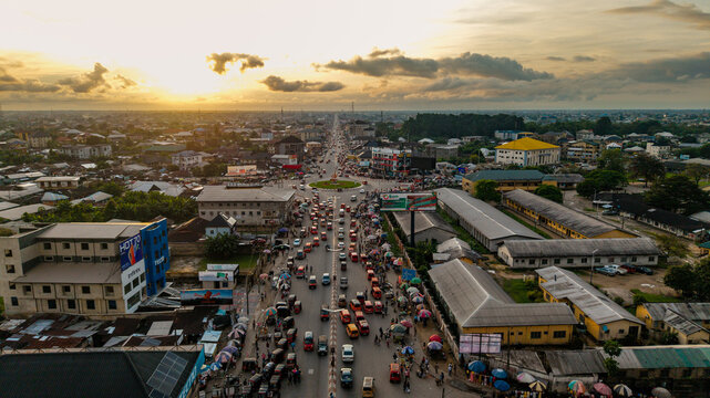 Aerial view of a busy roundabout with heavy traffic, street vendors, and urban buildings under a golden sunset sky in Uyo, Akwa Ibom, Nigeria.