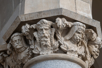 Intricately carved Renaissance stone column capitals featuring human heads and botanical motifs on Sukiennice Cloth Hall in the Main Market Square in Krakow, Poland. © Danica Chang