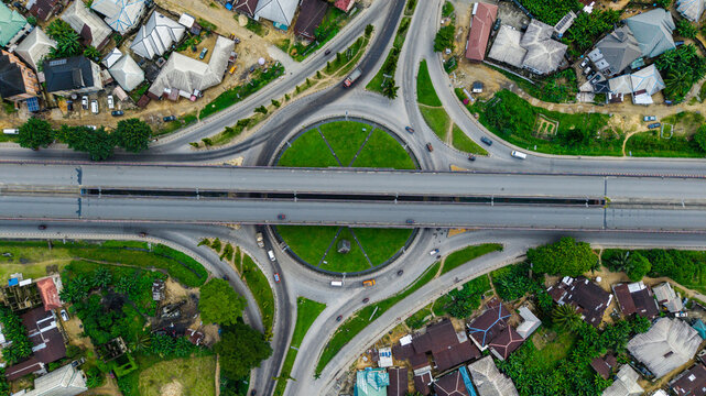Aerial view of a large roundabout with a central green space and an elevated highway bridge crossing over it, surrounded by residential buildings and vegetation in Uyo, Akwa Ibom, Nigeria.