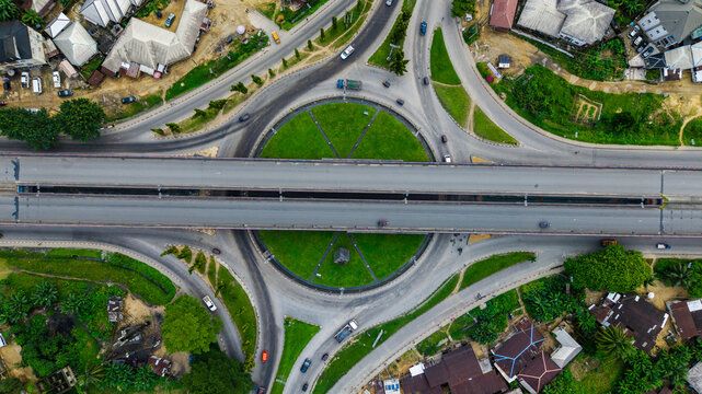 Aerial view of a large roundabout with a central green space and an elevated highway bridge crossing over it, surrounded by urban residential areas in Uyo, Akwa Ibom, Nigeria.