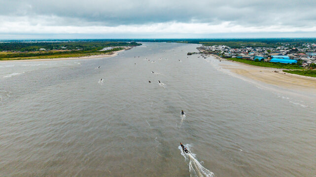 Aerial view of Ibeno Beach at the Kwa Ibo River estuary with small fishing boats navigating the water, sandy shores, and coastal settlement in Kwa Ibo, Akwa Ibom, Nigeria.