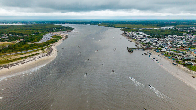 Aerial view of Ibeno Beach and the Kwa Ibo River estuary with small boats navigating the water, sandy shores, and coastal town buildings in Kwa Ibo, Akwa Ibom, Nigeria.