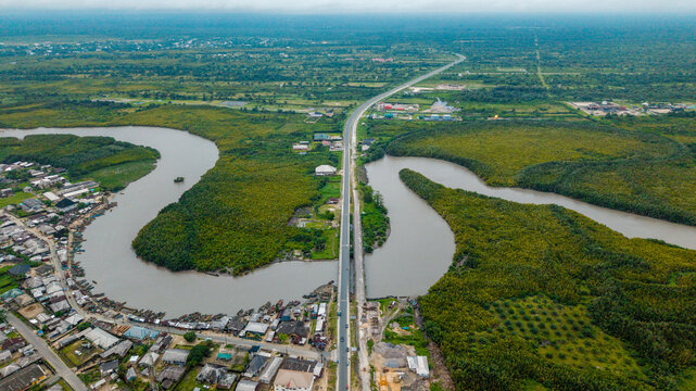 Aerial view of the Kwa Ibo River winding through lush mangrove forests and coastal vegetation, with a bridge crossing the water and a nearby settlement in Kwa Ibo, Akwa Ibom, Nigeria.