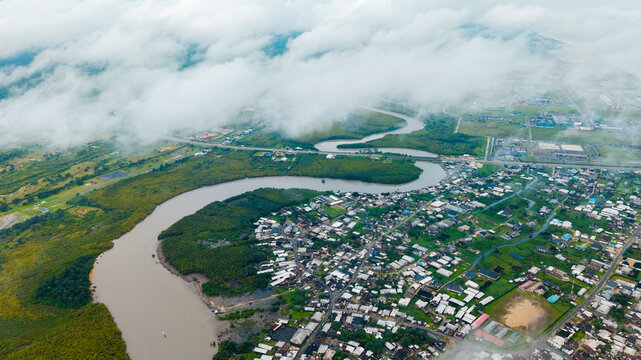 Aerial view of Ibeno Beach area with the winding Kwa Ibo River, lush mangrove forests, and coastal residential buildings under a cloudy sky in Kwa Ibo, Akwa Ibom, Nigeria.