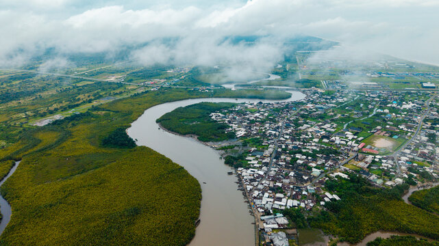 Aerial view of the winding Kwa Ibo River flowing through lush mangrove forests and a coastal settlement with dense housing under a cloudy sky in Kwa Ibo, Akwa Ibom, Nigeria.