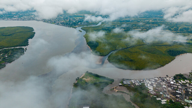 Aerial view of the Kwa Ibo River estuary with lush mangrove forests, winding waterways, and a small coastal settlement under a cloudy sky in Kwa Ibo, Akwa Ibom, Nigeria.