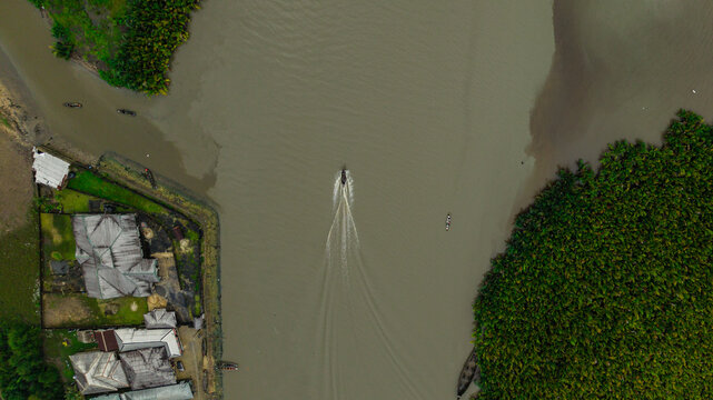 Aerial view of a small boat navigating the calm waters of the Kwa Ibo River, flanked by lush green vegetation and riverside buildings Kwa Ibo, Akwa Ibom, Nigeria.