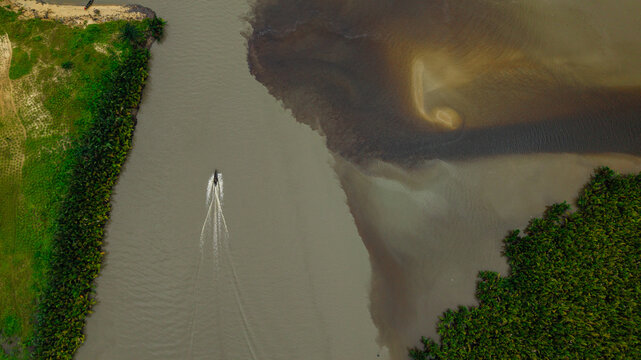 Aerial view of a small boat traveling along the Kwa Ibo River near Ibeno Beach, surrounded by lush mangrove forests and sandy riverbanks in Kwa Ibo, Akwa Ibom, Nigeria.