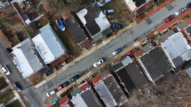Aerial view of a residential street featuring rows of houses with various roof types, parked cars along the road, and bare trees in a suburban neighborhood in Chester, Pennsylvania, United States.