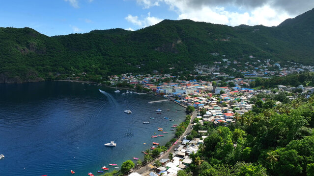 Aerial view of the coastal town of Soufriere nestled between lush green mountains and the Caribbean Sea, with colorful houses and small boats in the bay, Soufriere, Soufriere, Saint Lucia.