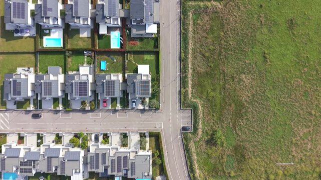 Aerial View of Suburban Houses: An overhead drone shot reveals a neat suburban neighborhood featuring modern houses with solar panels, swimming pools, and manicured lawns.