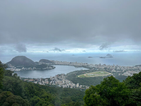 Scenic high-angle view over Rio de Janeiro on an overcast day, showing Rodrigo de Freitas lagoon, the Gavea hippodrome, lush rainforest, and the Atlantic Ocean.